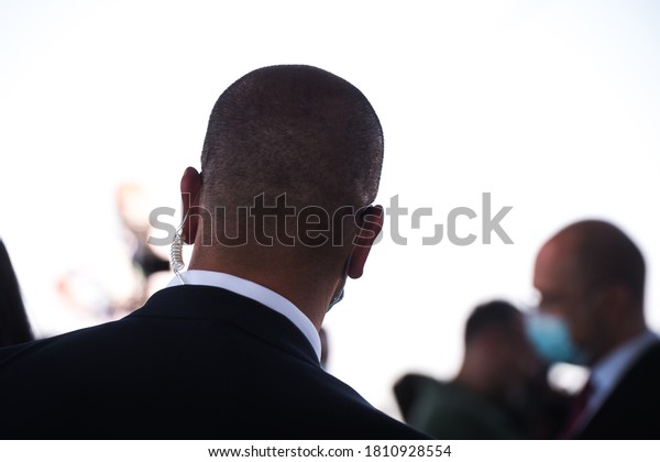 Security guard listening to his\
earpiece on event. Back of jacket showing. secret service guard.\
private bodyguard. man with earpiece in crowd. Black\
suit.