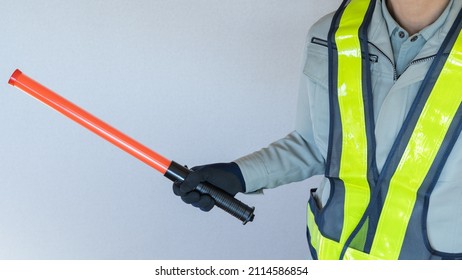 A Security Guard Man With A Red Stick.