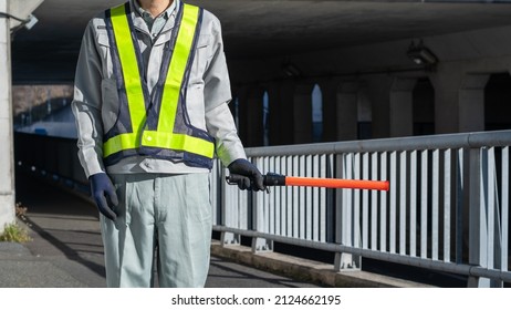 A Security Guard Man With A Red Stick.