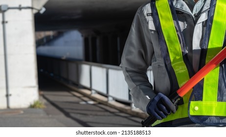 A Security Guard Man With A Red Stick.