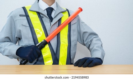 A Security Guard Man With A Red Stick.