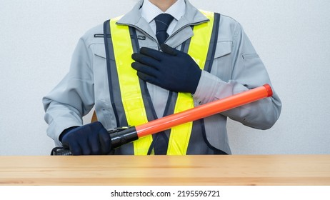 A Security Guard Man With A Red Stick.