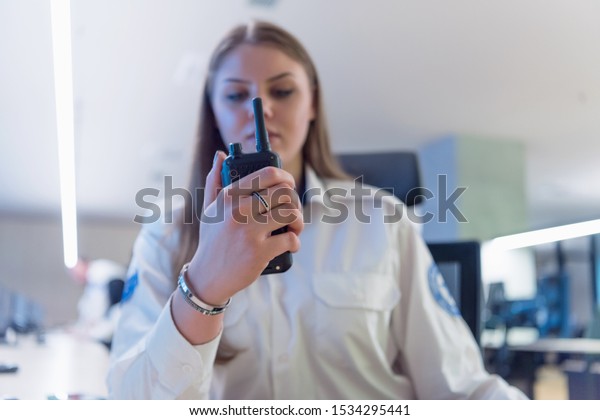 Security guard\
monitoring modern CCTV cameras in surveillance room. Female\
security guard in surveillance room. Female security guard holding\
portable radio in hand at\
workplace.