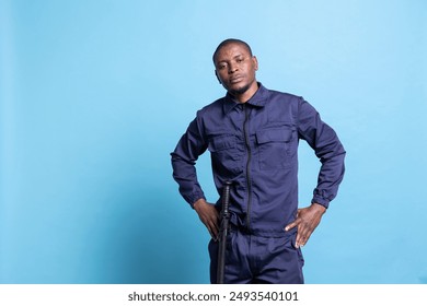 Security guard showing his authority by posing with hand on his hips against blue background, confident armed bodyguard. Male agent feeling proud in his work uniform while on duty. - Powered by Shutterstock