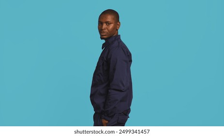 Security guard turning around after hearing suspect sounds during surveillance shift, ensuring protection. Portrait of man in uniform standing isolated with back against studio background, camera B - Powered by Shutterstock