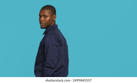 Security guard turning around after hearing suspect sounds during surveillance shift, ensuring protection. Portrait of man in uniform standing isolated with back against studio background, camera A - Powered by Shutterstock