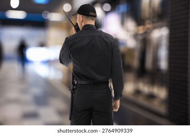 Security guard in uniform using portable radio transmitter at mall, back view
