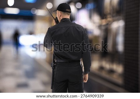 Security guard in uniform using portable radio transmitter at mall, back view