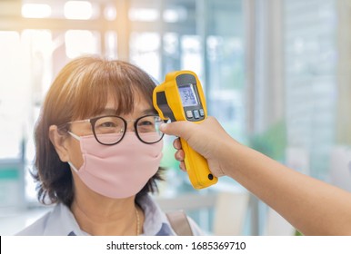 Security guard using digital medical electronic thermometer measures checking body temperature screening passengers protective preventing contagious diseases spread of coronavirus COVID-19 in airport 