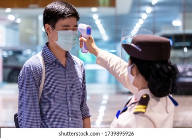 Security Guard Using Infrared Thermometer To Measure Body Temperature Check Asian People In  Protective Mask Before Access To Office Building For Against Epidemic Flu Coronavirus (CoVID-19) From Wuhan