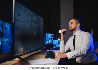 Security guard working night shift, communicating via radio and monitoring live surveillance feeds on multiple screens in a dark control room