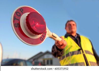 A security man is holding a red stop sign in his hands. He is stopping the traffic and navigating it in this small neighbourhood.