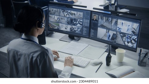 Security officer in headset controls CCTV cameras with AI facial recognition on PC. Female employee works in security control center. Computer monitors showing surveillance cameras video footage.