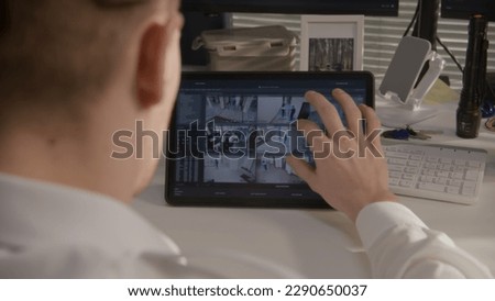 Security officer monitors CCTV cameras in coworking office on digital tablet computer. Modern program showing footage of surveillance cameras on screen. High tech security. Concept of social safety.