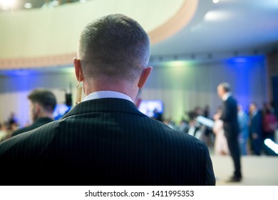 Security On Public Event. Secret Guard Service. Private Bodyguard With Earpiece Standing Among Crowd. Safety Of Govern And Business Meeting. Secret Service Agent Listening To His Earpiece, Side.