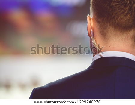 Security on public event. Secret guard service.  Private bodyguard with earpiece standing among crowd. Safety of govern and business meeting. Secret service agent listening to his earpiece, side.