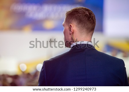 Security on public event. Secret guard service.  Private bodyguard with earpiece standing among crowd. Safety of govern and business meeting. Secret service agent listening to his earpiece, side.