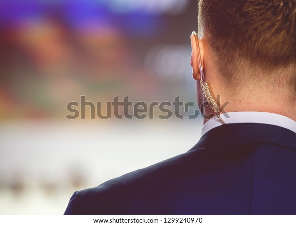 Security on public event. Secret guard service. 
Private bodyguard with earpiece standing among crowd. Safety of
govern and business meeting. Secret service agent listening to his
earpiece, side.
