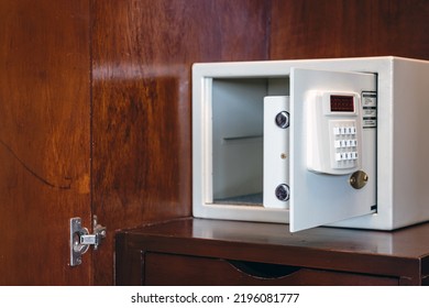 Security open metal safe with empty space inside in a wooden shelf. White safe box open door. Safe box with electronic lock in the hotel or home. Selective Focus on locking mechanism of small safes.
