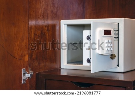 Security open metal safe with empty space inside in a wooden shelf. White safe box open door. Safe box with electronic lock in the hotel or home. Selective Focus on locking mechanism of small safes.