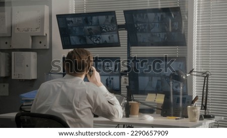 Security operator monitors office CCTV cameras on computers, uses walkie talkie. Modern software showing footage of surveillance cameras on screens. High tech security. Concept of social safety.