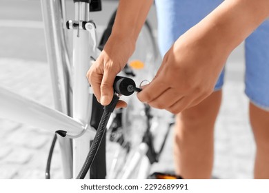 security, people and leisure - close up of woman opening cable lock and unfastening bicycle from parking rack on city street - Powered by Shutterstock