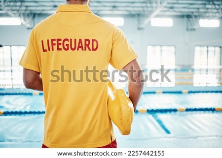 Security, safety or lifeguard by a swimming pool to help rescue the public from danger or drowning in water. Back view, trust or man standing with a lifebuoy ready with reliable assistance or support