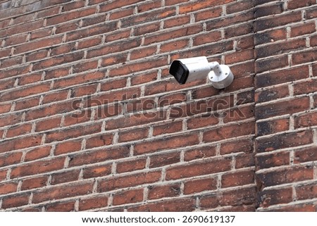 Security surveillance camera mounted on a weathered brick wall. Urban monitoring setup with industrial and rustic textures.
