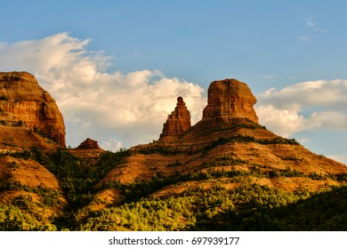 Sedona Arizona canyon bathed in sunlight variegated layers of red rock and vibrant colors with a bright blue sky and clouds in the background. - Shutterstock ID 697939177