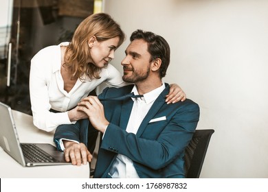 Seducing Colleagues In Office. Sexy Blonde Woman Flirting With Handsome Smiling Business Man Pulling Him By A Tie And Looking Into His Eyes. Tinted Image.