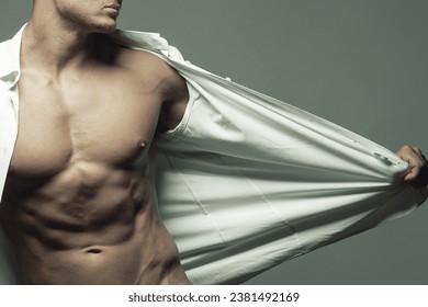 Seduction concept. Portrait of handsome muscular male model in classic shirt, pants posing over gray background, showing his perfect body. Clean skin. Text space. Studio shot