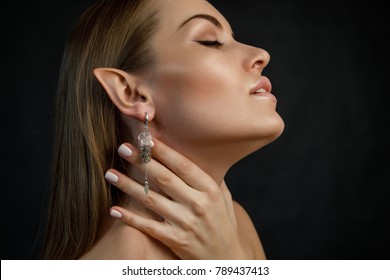 seductive young blonde woman with jewelry earring in elf ear  and hand on neck 