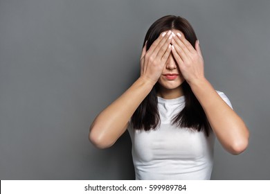 See no evil concept. Portrait of young scared woman covering eyes with hands while standing against gray studio background. Confused girl close eyes with palms ignoring something - Shutterstock ID 599989784