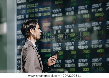 See the stock price board reflected on an outdoor electronic bulletin board with a smartphone in your hand, a man in a suit in his thirties in his thirties