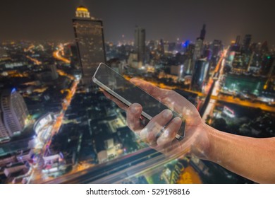 See Through Of Man's Hand Holding Mobile Phone On Blurred City Light At Night, Communication Technology Concept