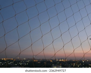 See through through plastic netting or nylon netting. (Used to prevent items from falling for elite residents or not to allow birds to nest.) During sunset, dark skies and bokeh created by street ligh