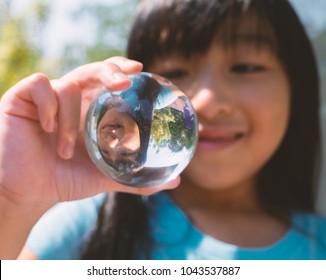 See yourself in another view. Close up of a Thai girl looking at a crystal ball that she is holding which showing upside down reflection of herself.