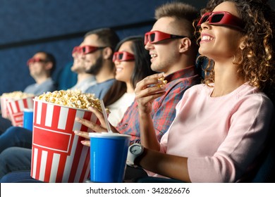 Seeing it in 3d. Friends sitting and eating popcorn together while watching movies at the cinema - Powered by Shutterstock