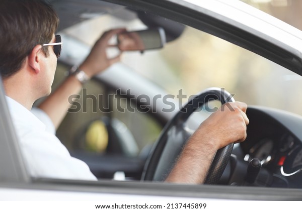 Seeing the road behind him. A man adjusting his\
rear view mirror while\
driving.