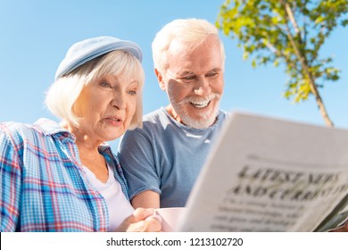 Seeing story. Grandmother and grandfather feeling happy seeing story about their grandchildren in newspaper