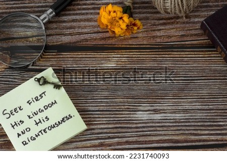 Seek first His kingdom and righteousness, handwritten verse on note with ancient key, magnifying glass, Bible Book on wooden background. Copy space. Christian hope, obedience, faith in God concept.