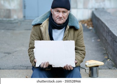 Seeking Help. Sad Exhausted Old-aged Man Is Sitting Outside And Holding A Cardboard Sign.