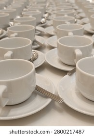 Seemingly endless rows of white teacups are set out for a large catered event.