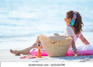 Seen From Behind 40 Year Old Woman In White T-shirt And Pink Shorts Sitting On Inflatable Mattress On The Beach.