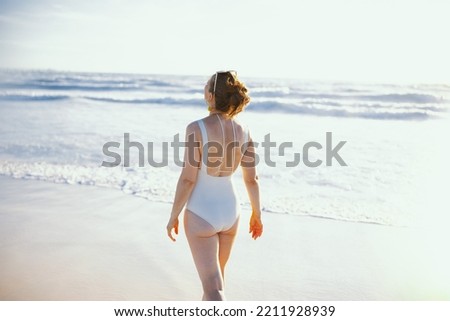 Seen from behind elegant 40 years old woman in white swimwear at the beach relaxing.