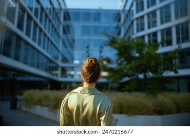Seen from behind middle aged woman employee near office building in green blouse.