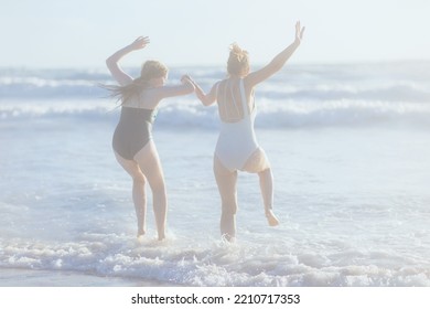 Seen From Behind Modern Mother And Child At The Beach In Swimwear Jumping.