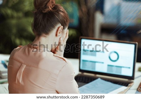 Seen from behind modern woman with documents and laptop having headache in modern office.