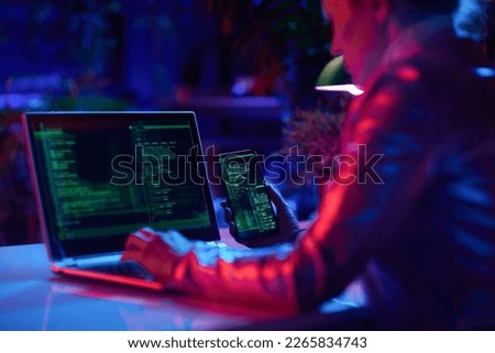 Seen from behind modern woman with laptop and smartphone protecting network against cyberattack from hackers on internet in modern office.