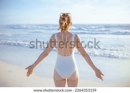Seen from behind modern woman in white swimsuit at the beach relaxing.